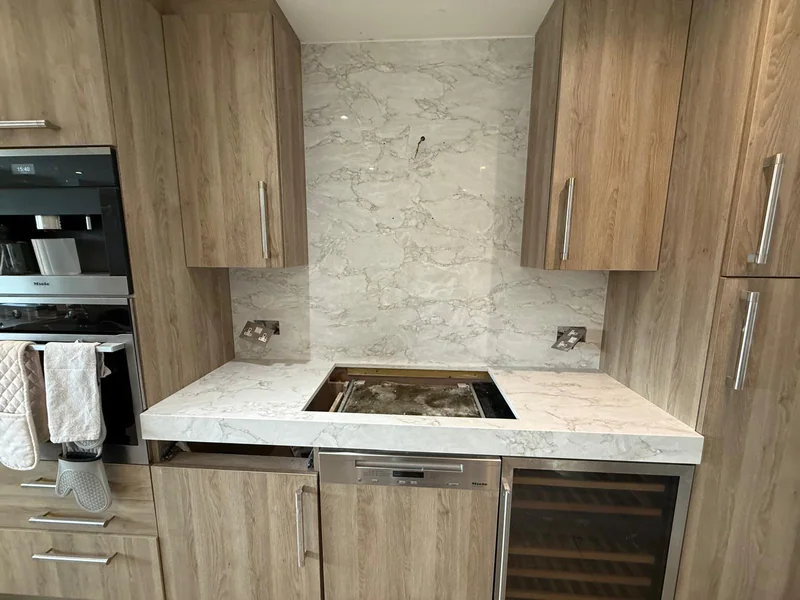 Matching veined worktop with a hob opening and tall splashback between timber cabinets